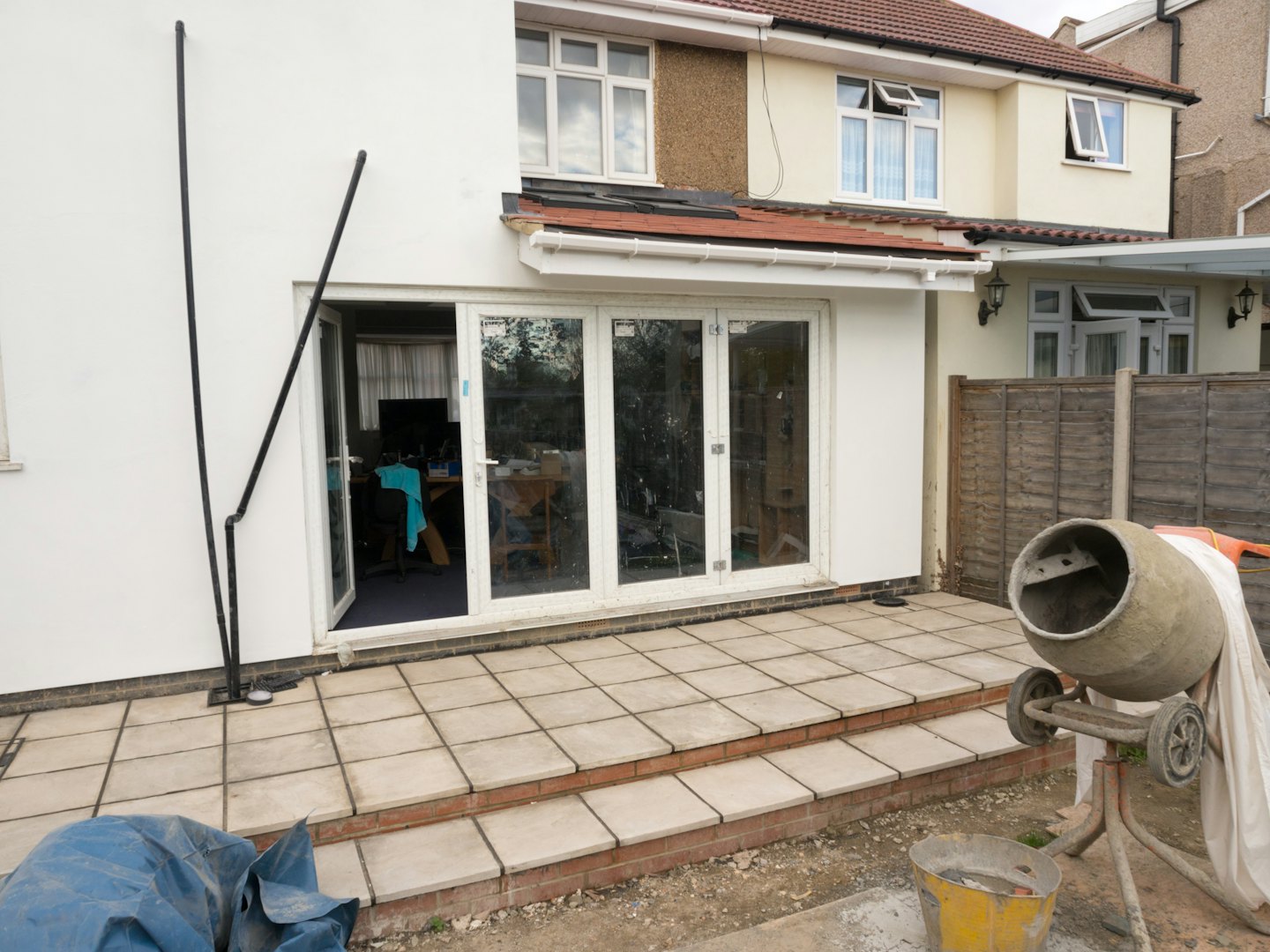 Renovation work continues outside a house with a white extension.