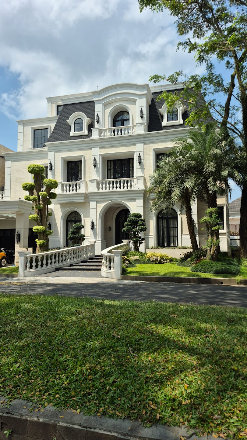 Grand luxury house with manicured gardens and tall palm trees.